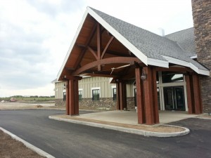 Custom designed timber frame entry and porte cochere with adzed finish by Log and Timber Works Saskatchewan
